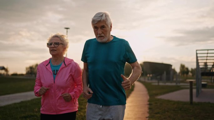 在日落时分，在公园的行人径上穿着运动服慢跑的长者夫妇
