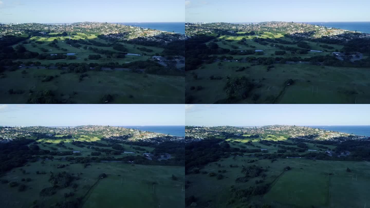 无人机飞过橄榄球场，俯瞰绿色风景的Bluff高尔夫球场，背景是道路分割和海洋