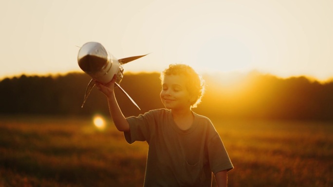 快乐的小男孩在夏天的草地上玩手工玩具火箭在日落的时候，快乐的时刻