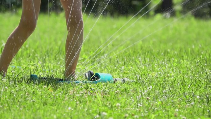 孩子们的脚被草坪上的洒水器喷出来的水柱浸湿的特写