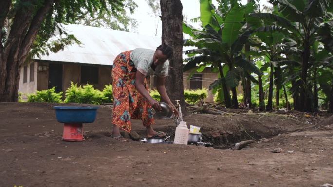 慢镜头的女人清洁餐具。一位女士正在户外洗盘子。她在香蕉农场附近。