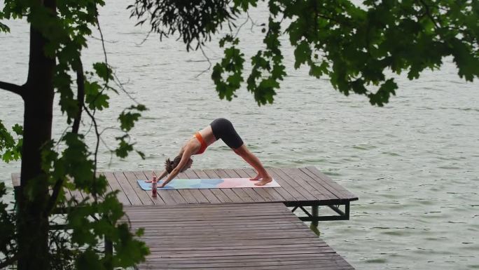 在湖边运动的女人。在水边的木码头上做瑜伽柔韧性练习