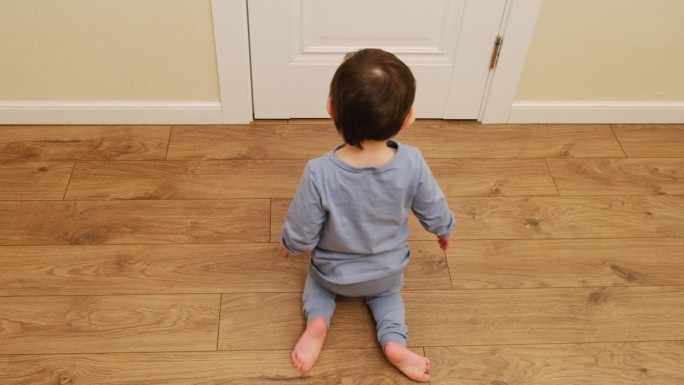 有趣的婴儿坐在地板上跪着爬。一个孩子在家里的客厅里异常地弯着腿走路。2岁左右(1岁9个月)