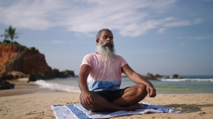 在海边天堂岛的沙滩上，老人在海浪声中冥想，坐着莲花式。在异国情调的海岸，黑人男高年级学生盘腿练习瑜伽