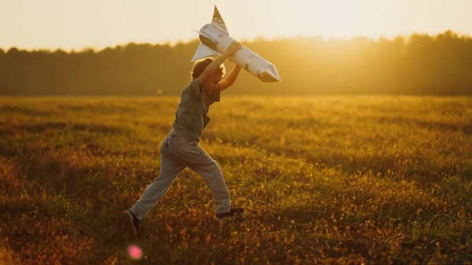 小梦想家男孩拿着手工火箭，在夏天跑过草地，侧视图，慢动作