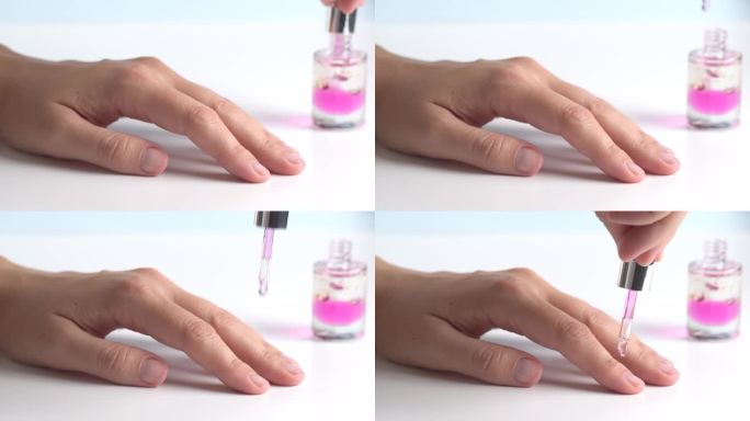 滋润表皮的粉色油。女人关心手和指甲，近距离。一位女士在浅色背景下用移液管向角质层上涂抹油脂。健康指甲