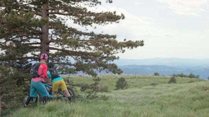 两个女人骑山地车休息，坐在山顶的草地上