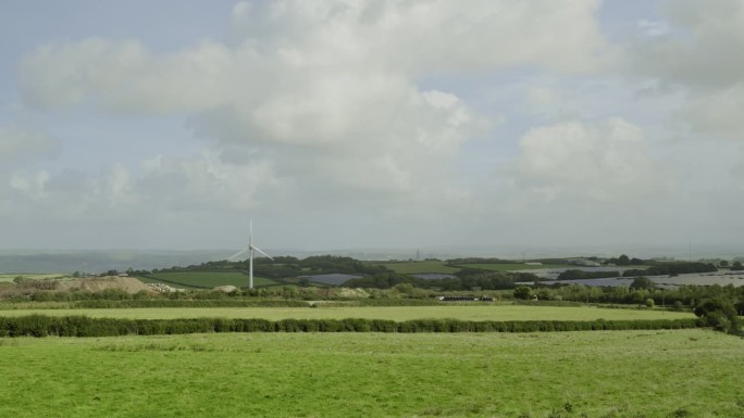 风力涡轮机站在德文郡绿色的田野上，蓝天白云，静拍。