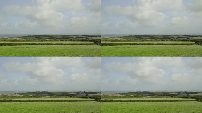 风力涡轮机站在德文郡绿色的田野上，蓝天白云，静拍。