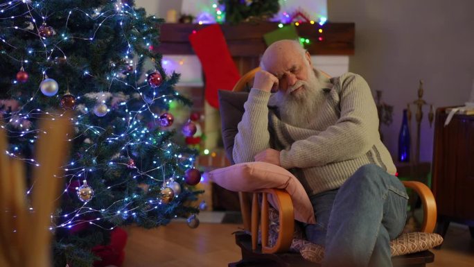一位老人在圣诞树旁的摇椅上抱着枕头睡着了。