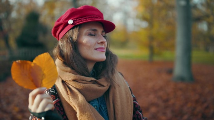 快乐的年轻女子戴着红帽子，戴着秋叶，围着围巾
