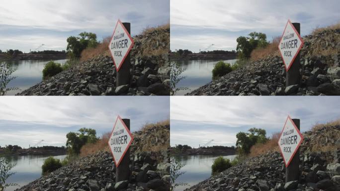 阴天下河岸上写着“浅危岩”的警告危险路牌