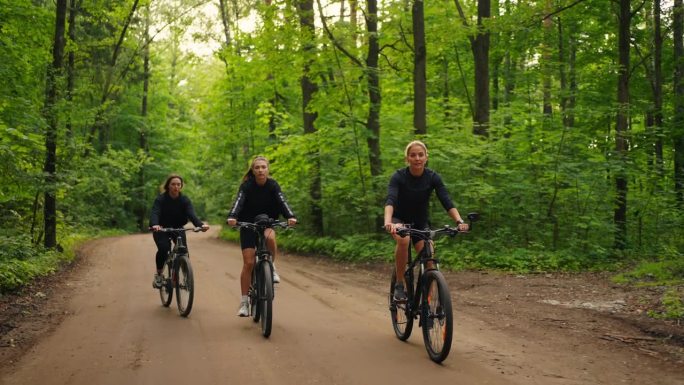 三个年轻的女人在美丽的森林里骑自行车，阳光明媚的日子，快乐的女孩玩得很开心