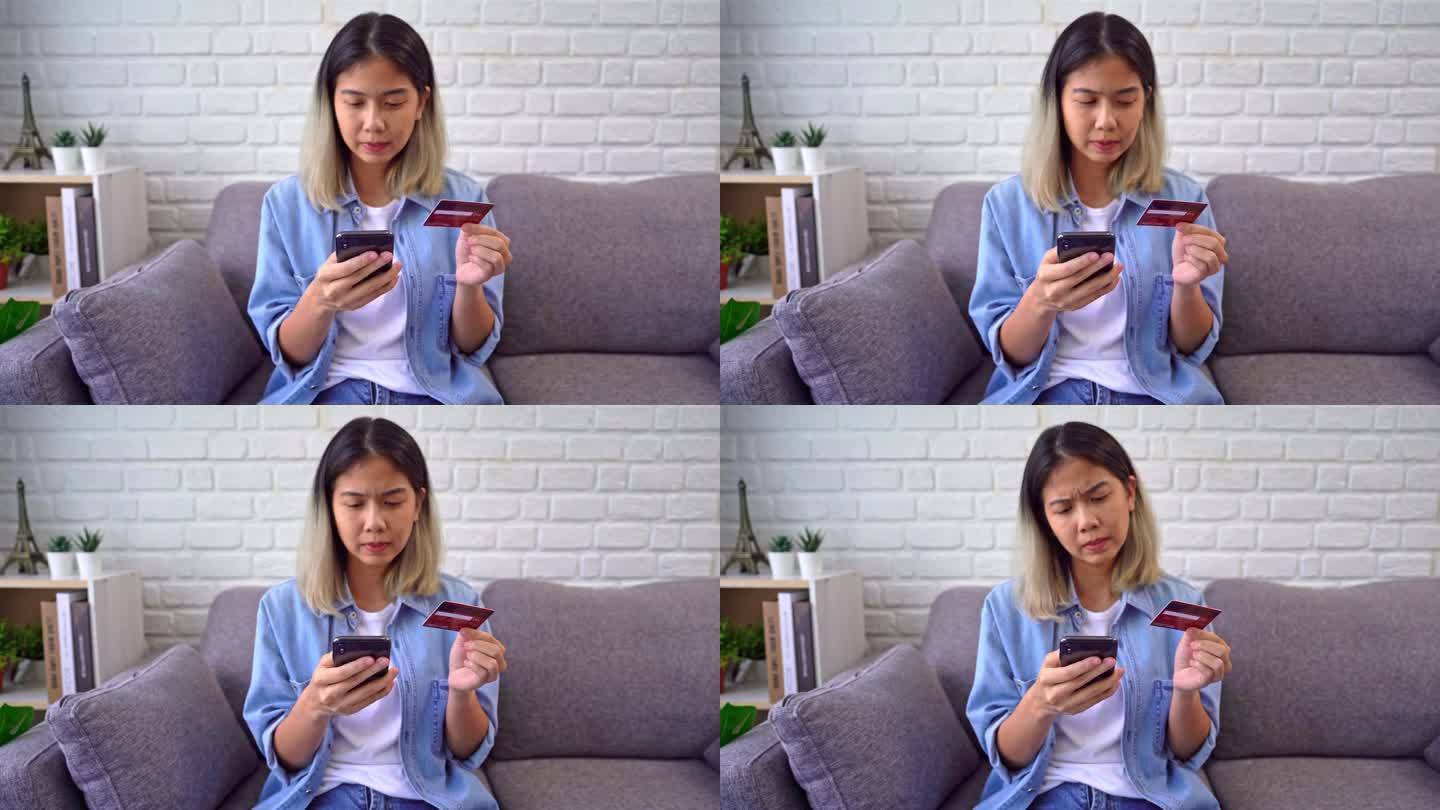 亚洲女性坐在沙发上拿着信用卡用手机尝试通过电子银行应用程序支付由于资金不足，没有钱而遇到问题。不成功