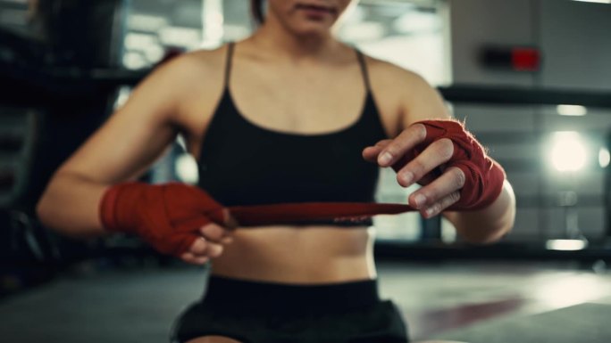 女拳手用红色的拳击绷带包扎双手，在健身房进行自由搏击训练。