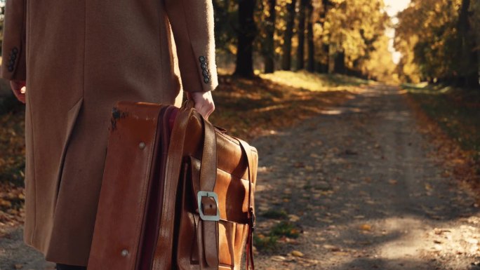 秋日里，穿着复古大衣、提着旅行箱走在路上的时尚女子
