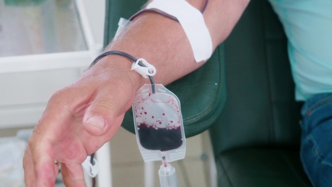 献血者坐在椅子上，在输血站献血。手拿针的特写视频。志愿者献血。