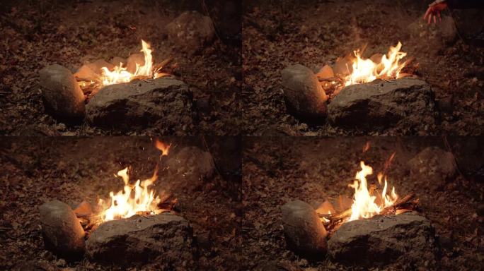 一堆石头围成的火正在燃烧。柴火被添加到火中，火花在黑暗中飞舞