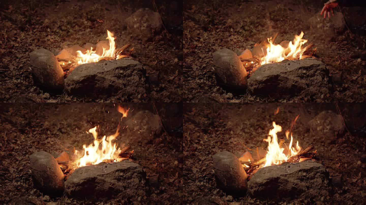 一堆石头围成的火正在燃烧。柴火被添加到火中，火花在黑暗中飞舞