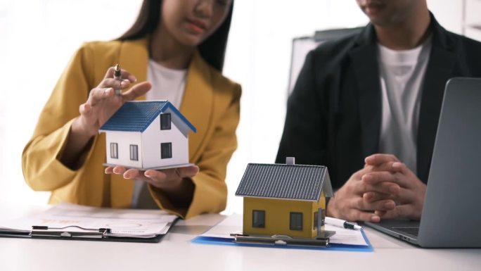 房地产经纪人提供购买或租赁房屋的合同。商人拿着模型小楼和财产保险在房屋销售处的桌子上