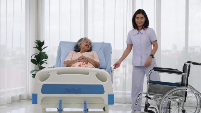 一名护士将一名亚洲老人从轮椅上抬到床上，他的腿在一次事故中受伤。