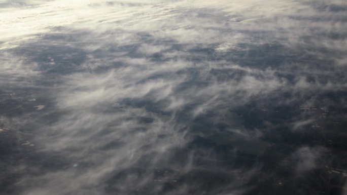从飞机窗口鸟瞰地球。在地球上空飞行的飞机上，以电影般的慢动作俯视地球上日落时的云朵。