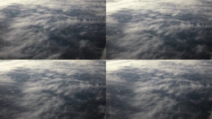 从飞机窗口鸟瞰地球。在地球上空飞行的飞机上，以电影般的慢动作俯视地球上日落时的云朵。