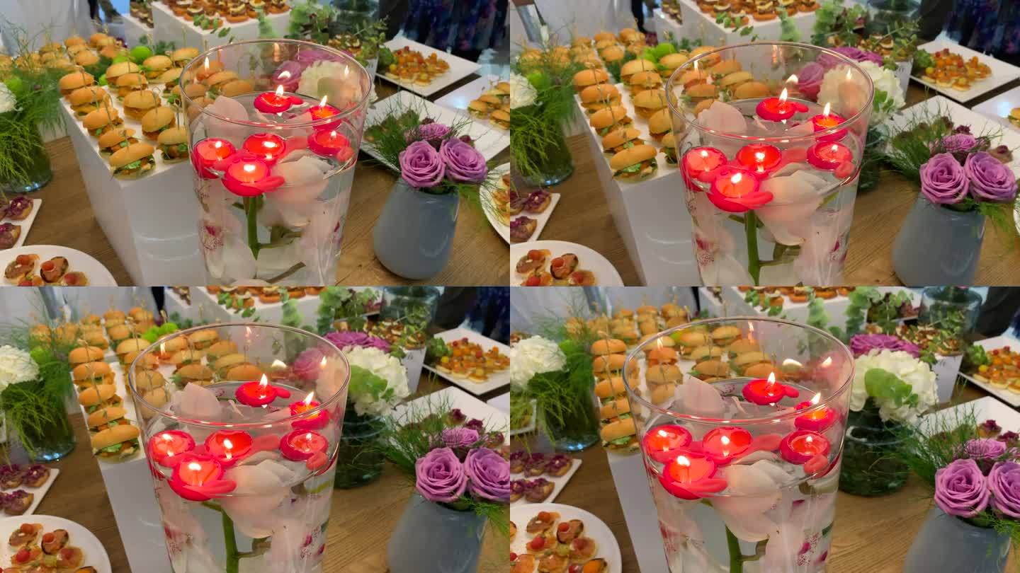 桌子上摆放着各种开胃菜和装饰着鲜花的小吃，还有一个装有漂浮蜡烛和一株浸没在水里的兰花的罐子。
