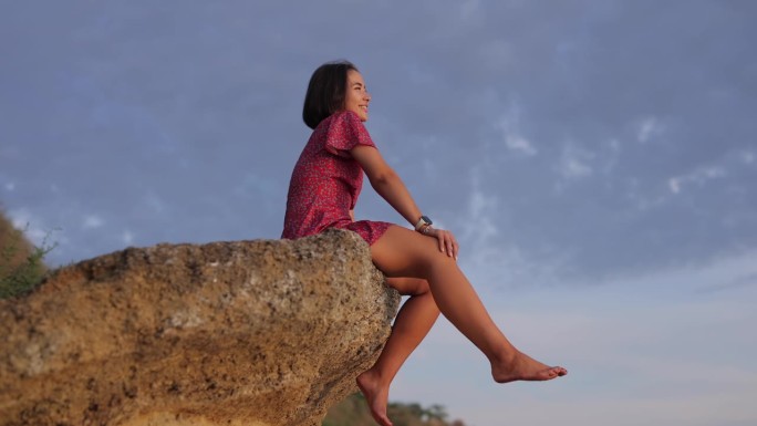 一个快乐的女人坐在一块石头上，背景是天空