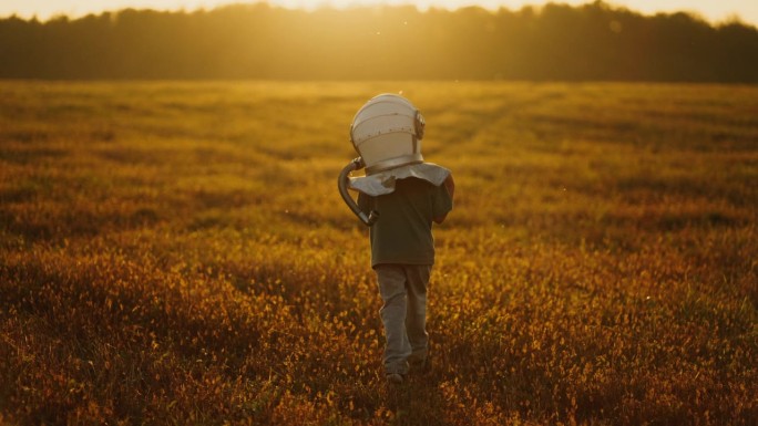 幻想和梦想太空旅行，戴着太空头盔的小男孩独自走在草坪上