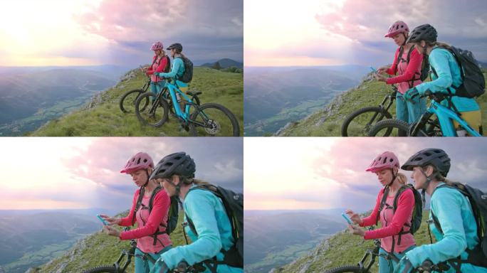 两个女山地自行车手站在山上看手机上的地图