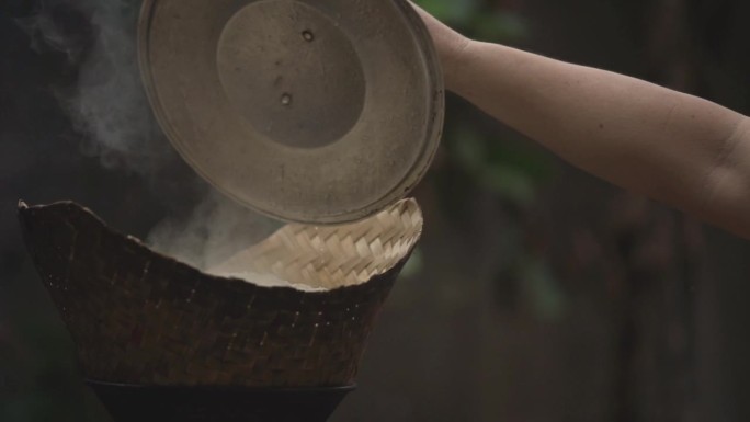 一个女人的手打开了蒸笼的盖子，蒸笼用烟和热蒸汽蒸糯米。