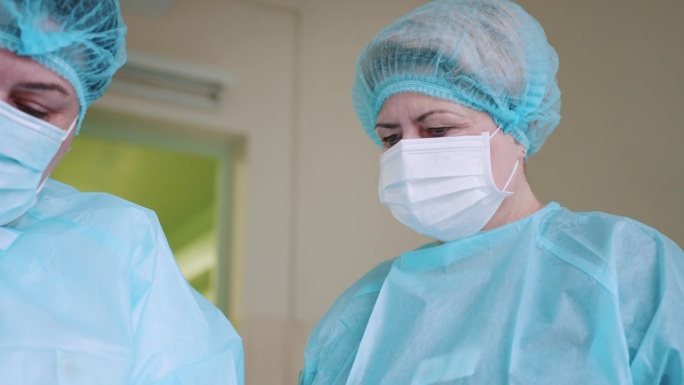戴口罩的医生。身穿医疗服的女护士的低角度镜头。穿着工作服的医生画像。手术室低角度拍摄，助手在手术中向