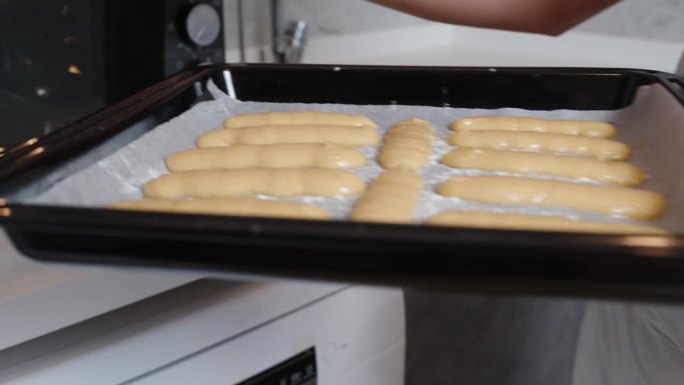 做泡芙的泡芙糕点放在烤盘上，女人把它放进烤箱。缓慢的运动。