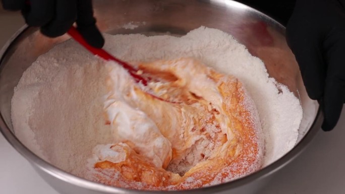 糕点师将硅胶刮刀和橙色面团混合在一个不锈钢碗里，用于制作法式甜点马卡龙或马卡龙，这是制作蛋糕的过程。