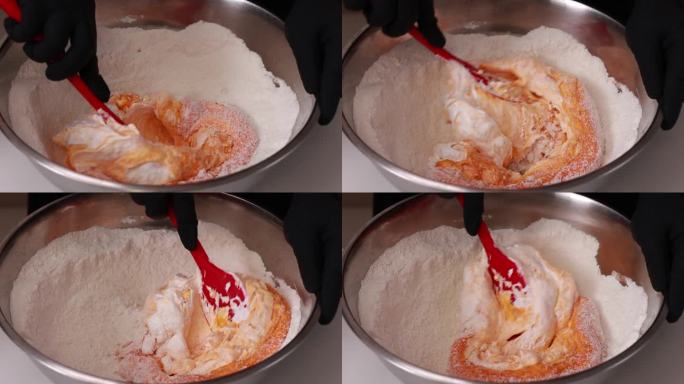 糕点师将硅胶刮刀和橙色面团混合在一个不锈钢碗里，用于制作法式甜点马卡龙或马卡龙，这是制作蛋糕的过程。