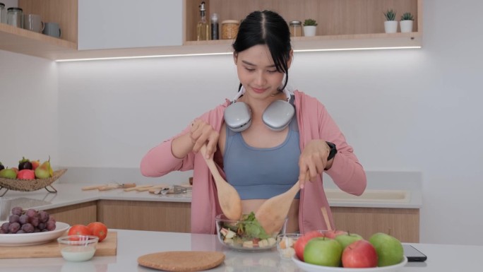 看起来很健康的年轻亚洲女人他高兴地把蔬菜沙拉扔到盘子里。