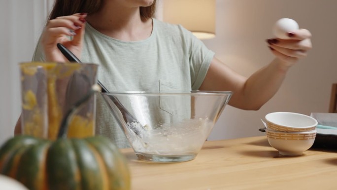 南瓜饼干食谱。女人把鸡蛋敲进碗里。