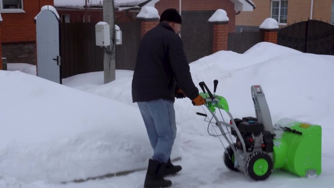 冬天，一个男人在房子的院子里清理积雪。一名男子用吹雪机清理积雪
