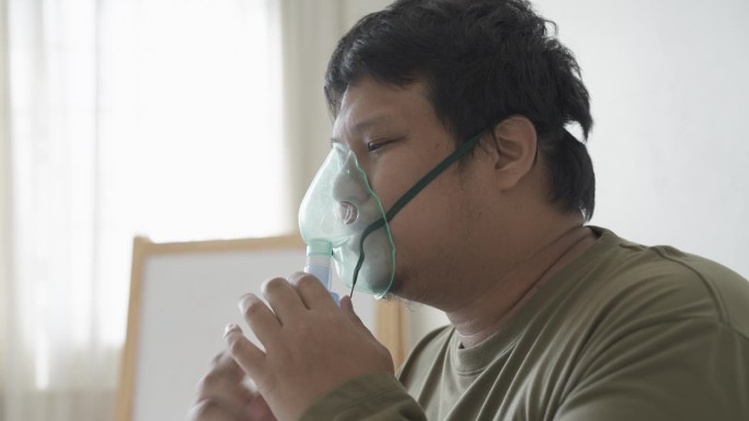 一名亚洲男子在卧室里用雾化器治疗哮喘