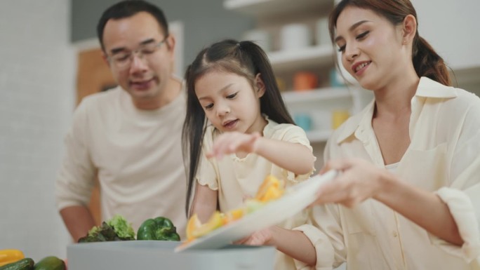 快乐的亚洲家庭在快乐厨房一起烹饪:父母教孩子制作新鲜蔬菜沙拉的艺术。