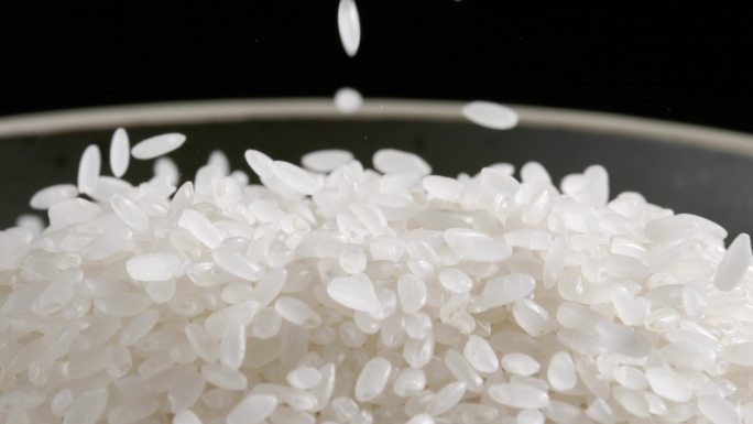 在黑背景上大米洒落到白色碗中