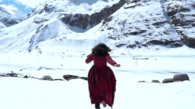 印度女孩穿着红色长袍，在印度拉胡尔的西苏雪山上快乐地奔跑。享受寒假的女孩。冬天山里穿裙子的女人。