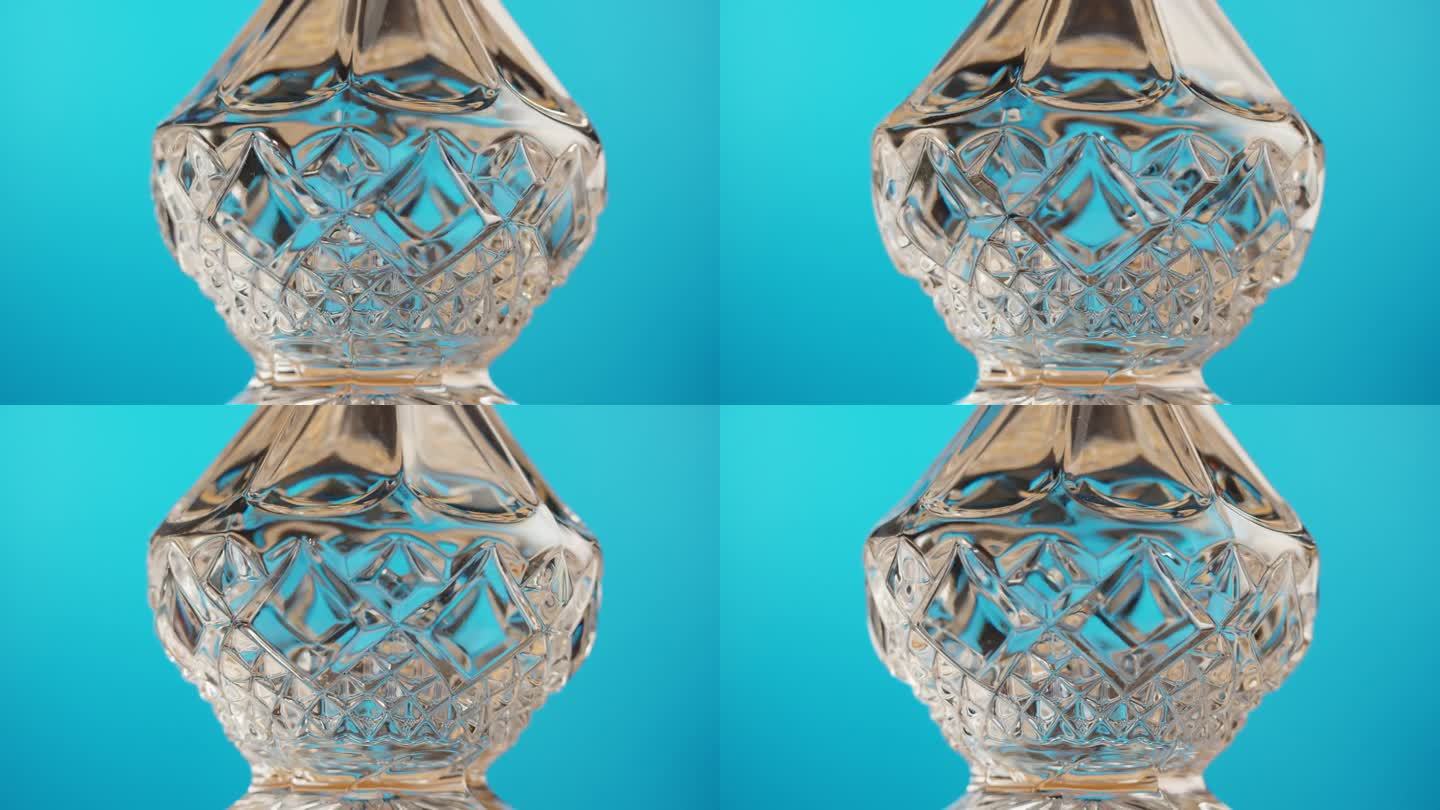 空水晶酒瓶特写。透明玻璃在蓝色背景上旋转。高档酒瓶，酒精饮料，玻璃器皿。