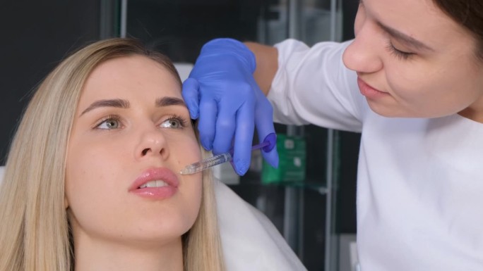 一位专业的美容师在一位年轻的金发女郎的嘴唇上打针。