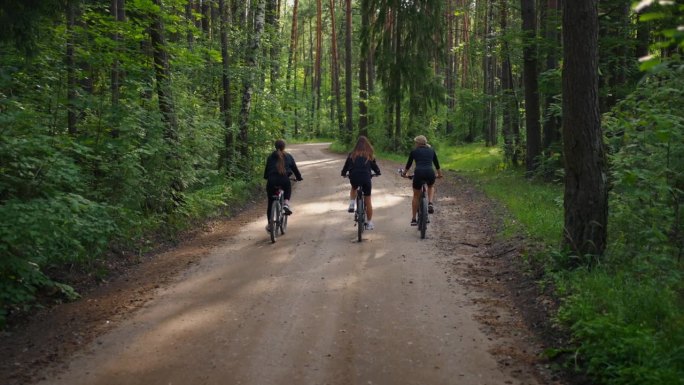 三个年轻的女孩朋友在夏天的森林里骑自行车，后景，积极的消遣