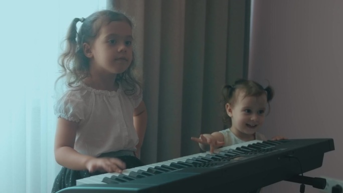 白人年轻的音乐家女孩孩子在家里的音乐教育中进行有趣的活动，演奏钢琴音乐课。蹒跚学步的妹妹也想玩。姐妹