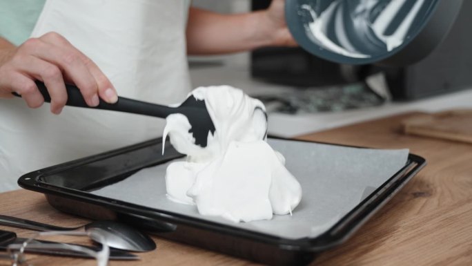 在一个特写镜头中，糕点师正在将蛋白霜淋在覆盖着羊皮纸的烤盘上。