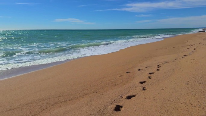 走在没有人的沙滩上，前景是沙滩上的脚印，流畅的运动伴随着大海