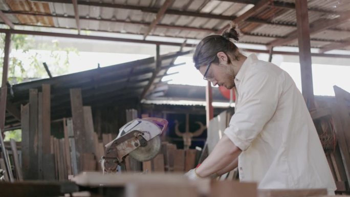 专家男木匠活跃在一家木材厂用电动机器锯木头制作家具。工人戴手套和口罩工作，以防止灰尘和事故。概念蓝领